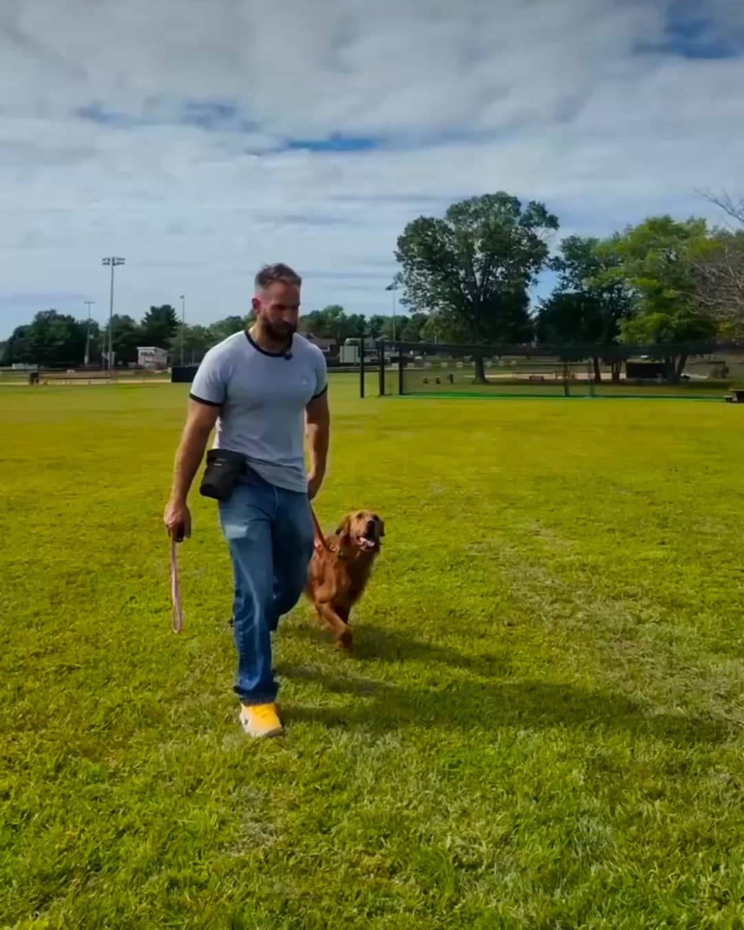 Trainer walking a golden retriever at heel across a training field